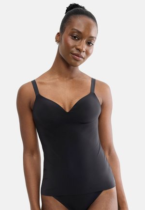 Woman with dark skin and hair in a bun wearing a fitted black camisole and black underwear, looking at the camera with a soft smile.