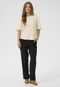 Krémový texturovaný, oversized top s krátkým rukávem v kombinaci s černými kalhotami rovného střihu. Hnědé nazouvací boty a jednoduchý náramek dokončují look.