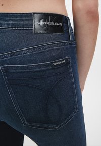 Jeans de mezclilla de lavado oscuro con un parche de cuero de Calvin Klein Jeans en la parte posterior, con sutiles detalles de costura y dos bolsillos traseros.