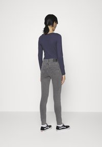 Pantalones vaqueros ajustados grises con cintura alta, bolsillos traseros y un parche negro. Combinados con una camiseta de manga larga azul marino y zapatillas negras.