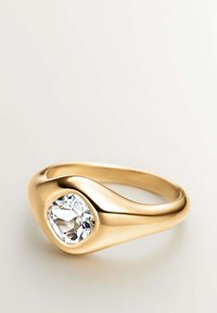 Anillo de oro con una piedra preciosa redonda y facetada, engastada en una banda suave y curvada, que resalta un diseño minimalista y moderno.