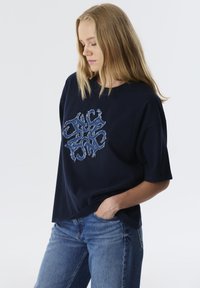 Marineblauwe oversized t-shirt van katoen, met een gestructureerd blauw borduurdesign in het midden. Korte mouwen en een relaxte pasvorm.