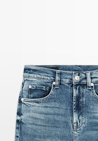 Jean en denim bleu moyen, avec poches avant, braguette zippée avec bouton et légère décoloration sur le tissu.