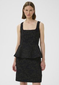 Robe peplum noire avec un décolleté carré, présentant une texture florale et un design superposé. Le tissu a un subtil éclat et une silhouette structurée.
