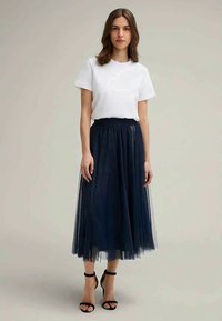 Navy tulle midi skirt paired with a white cotton t-shirt. The skirt features a fitted waistband and layered, sheer texture. Black ankle straps complete the look.