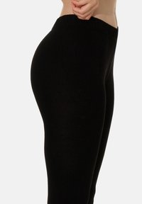 Leggings neri con un design aderente, vita elasticizzata e texture morbida, che mettono in risalto una silhouette liscia. Nessun motivo o hardware visibile.