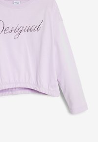 Lila cropped pulóver hosszú ujjakkal, kerek nyakkivágással, elöl strasszokkal díszítve, rajta a "Desigual" felirattal. Ráncolt szegély.