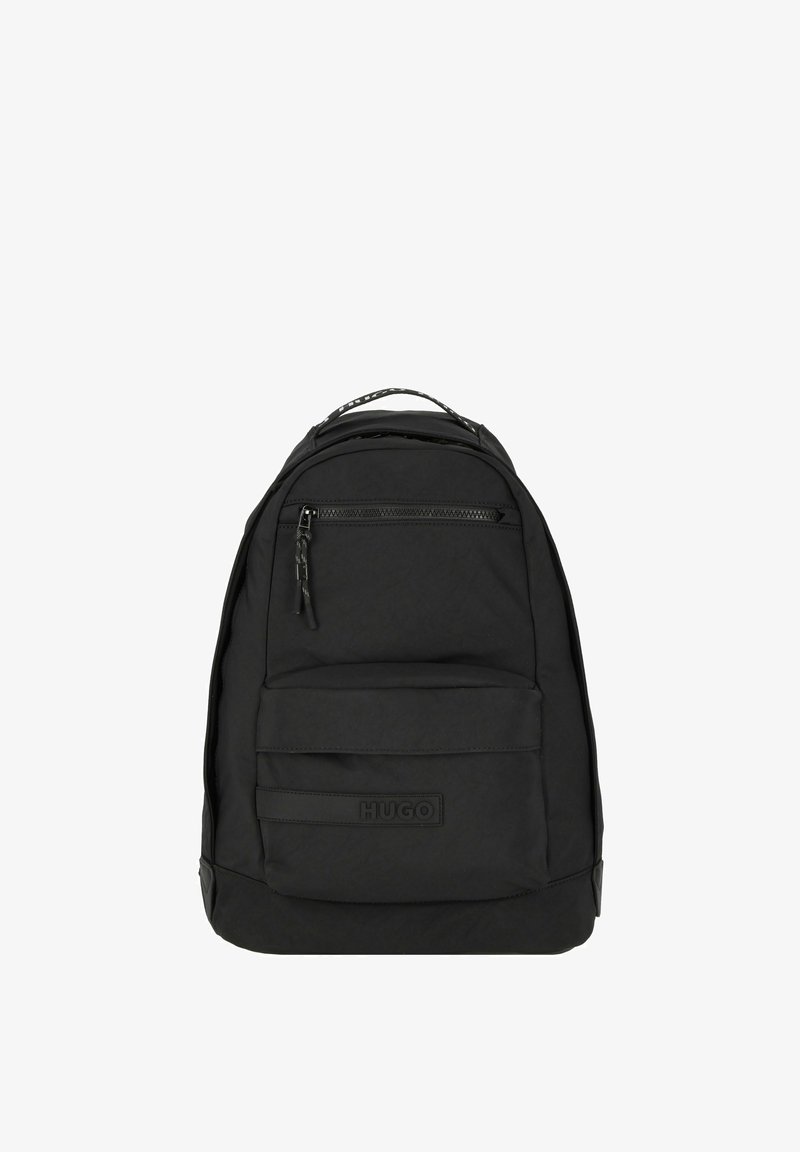 Mochila negra hecha de tela texturizada, con un asa superior, un bolsillo con cremallera en la parte frontal y un parche con el logo. Forma compacta y redondeada para facilitar el transporte.