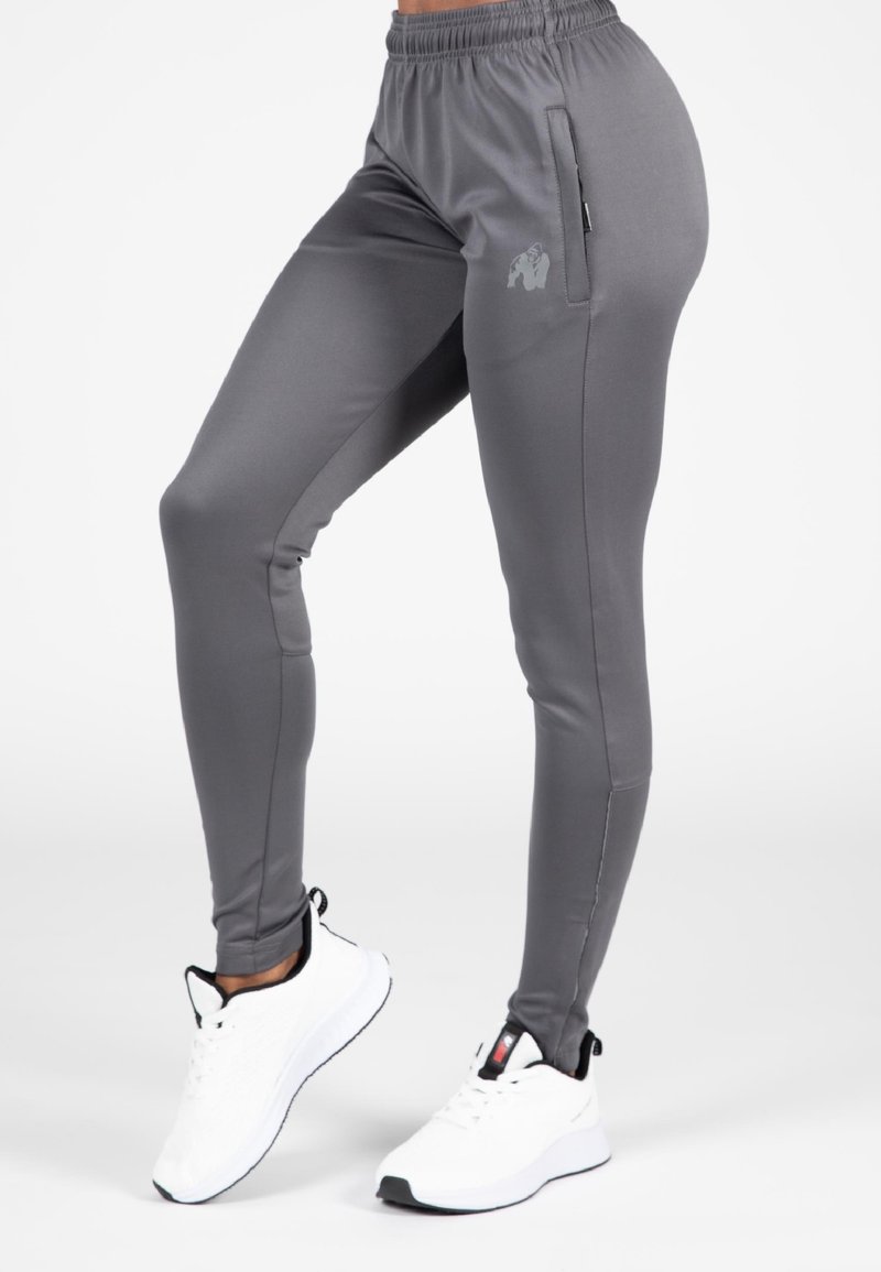 Grijze sportleggings met een gladde textuur, voorzien van een zijzak en een subtiel logo. Gecombineerd met witte sportschoenen.