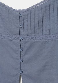 Haut bleu sans manches avec des plis verticaux, un bord en dentelle au niveau de l'encolure et de la taille, et une rangée centrale de six boutons.