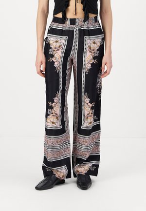 Pantalones negros con un estampado que combina diseños florales y de paisley, con perneras anchas y bordes blancos contrastantes, hechos de una tela suave y lisa.
