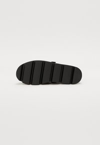 Suela de zapato negra con una superficie texturada, que presenta múltiples ranuras horizontales para mayor agarre y soporte. Diseño plano, sin marcas visibles.