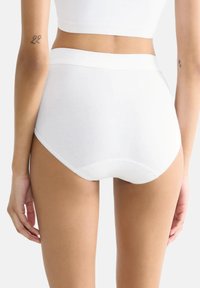 Culotte en coton blanc taille haute avec une texture lisse, une ceinture large et sans coutures visibles ; s'ajuste bien au corps.