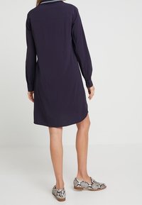 Marinblå skjortklänning med långa ärmar, krage och rundad nederkant. Bärs med mönstrade skor med en ormdesign.