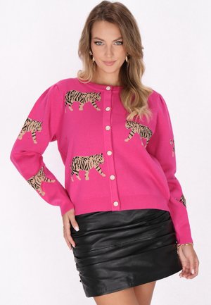 Cardigan rosa con motivi a tigre marroni, bottoni frontali e maniche a sbuffo, abbinato a una gonna in pelle nera plissettata.