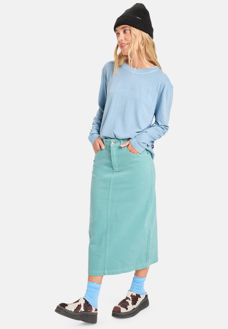 Lichtblauw overhemd met lange mouwen, mintgroene spijkerrok, zwarte beanie, blauwe sokken en schoenen met koeienprint. Focus op zachte texturen en een casual ontwerp.