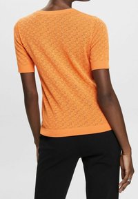 Kortärmad orange stickad tröja med ett strukturerat mönster och hålmönsterdetaljer. Rundad halsringning och ribbade mudd vid ärmar och nederkant.