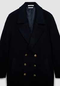Cappotto in misto lana doppiopetto di un profondo blu navy. Presenta un ampio rever a punta, due tasche frontali e bottoni dorati. Fodera interna liscia.