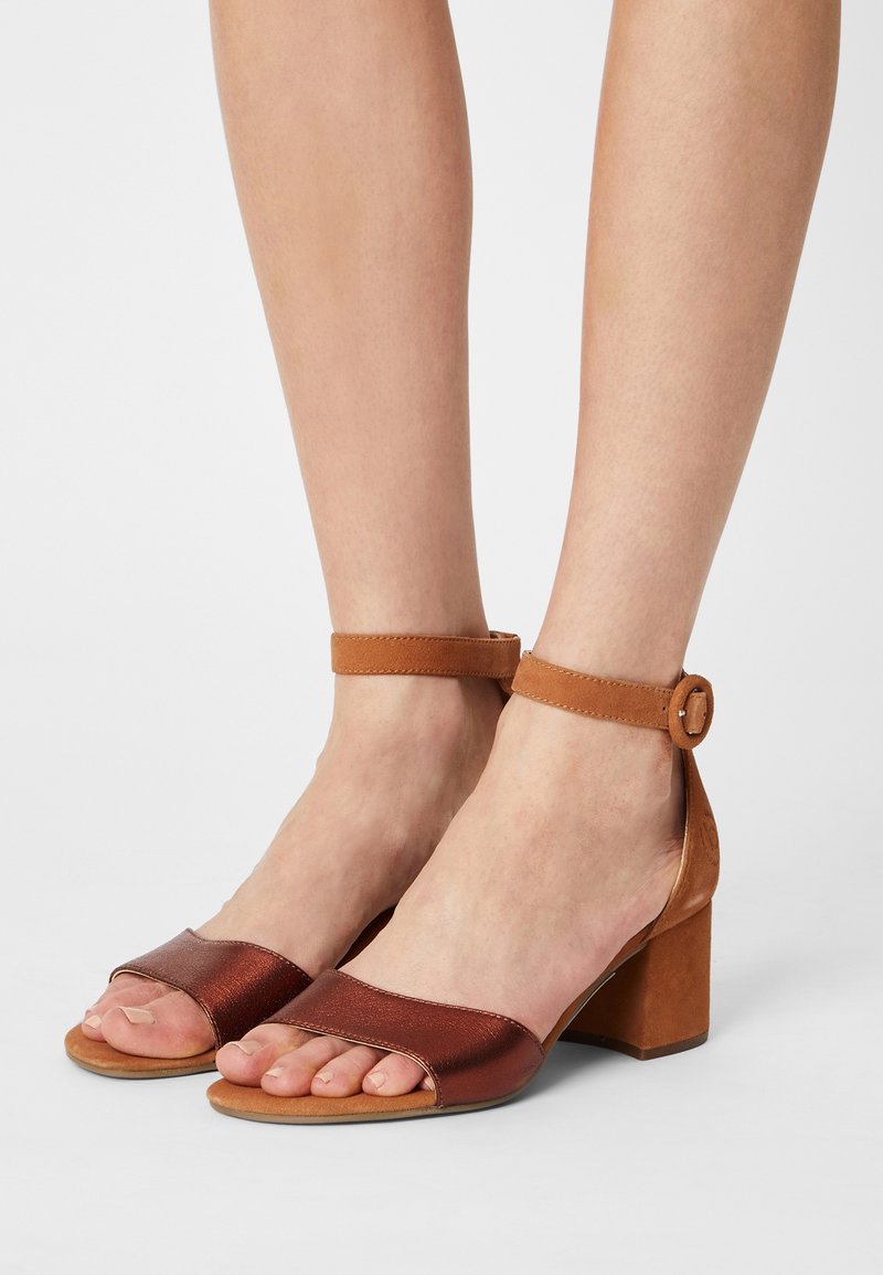 Sandales à talons marron avec une sangle de orteil en bronze métallique et une sangle de cheville beige dotée d'une boucle. Talon bloc pour plus de stabilité.