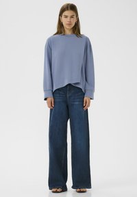 Felpa azzurra chiara con cucitura diagonale, abbinata a jeans blu scuri a gamba larga. Design semplice con maniche lunghe e vestibilità morbida.