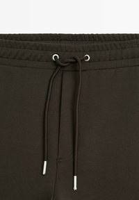 Dunkelgrüne Jogginghosen mit einem elastischen Bund, verstellbarem Kordelzug und silbernen Metallbeschlägen. Weiche Textur, keine sichtbaren Muster.