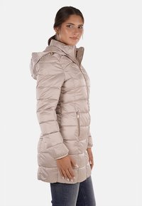 Giacca puffer beige chiaro con zip frontale, cappuccio e motivo trapuntato diagonale. Presenta due tasche laterali con chiusura a zip.