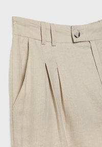 Pantalon beige taille haute avec plis, passants de ceinture, poches latérales et fermeture par un bouton unique à la taille.