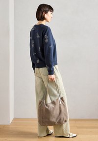 Ναυτικό φούτερ με κεντημένα σχέδια, ανοιχτό μπεζ παντελόνι φαρδιάς γραμμής και μαλακή σουέντ τσάντα σε ταμπά απόχρωση με γκρίζες λωρίδες. Επίπεδες παπούτσια με αντίθετα άκρα.