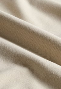 Beežist puuvillasest kangast, millel on sile tekstuur, õrnade soonte ja voltidega, pehme läikega, pehmetes rippuvates kihtides.