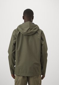 Veste imperméable verte olive avec capuche, présentant une coupe décontractée et une texture lisse, vue de dos.
