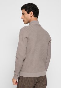 Gebreide trui in licht taupe, met een hoge kraag en een geribbelde textuur. Getailleerd ontwerp met een effen basis en subtiele zijdetails.