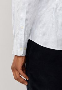 Witte shirt met blauwe stippen, voorzien van een knoopmanchet en textiel met structuur, gecombineerd met donkere corduroy broek.