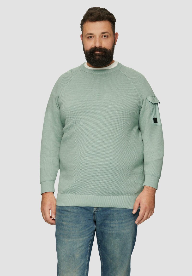 Mintgroene sweater van textiel met een reliëfstructuur, geribde manchetten en onderrand, raglanmouwen en een zakdetail aan de zijkant. Gecombineerd met een spijkerbroek.