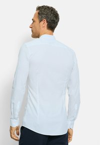 Witte blouse met lange mouwen en een aansluitend ontwerp. Voorzien van een klassieke kraag, knoopmanchetten, een gladde textuur en een rechte zoom. Achteraanzicht.