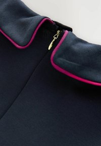 Abito blu navy con colletto arrotondato e bordo rosa. Include una cerniera dorata sul retro. Tessuto testurizzato con una finitura liscia.