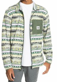 Chaqueta de forro polar con un patrón tribal multicolor en verde, amarillo y gris. Incluye un bolsillo de parche verde y un cierre totalmente de cremallera.