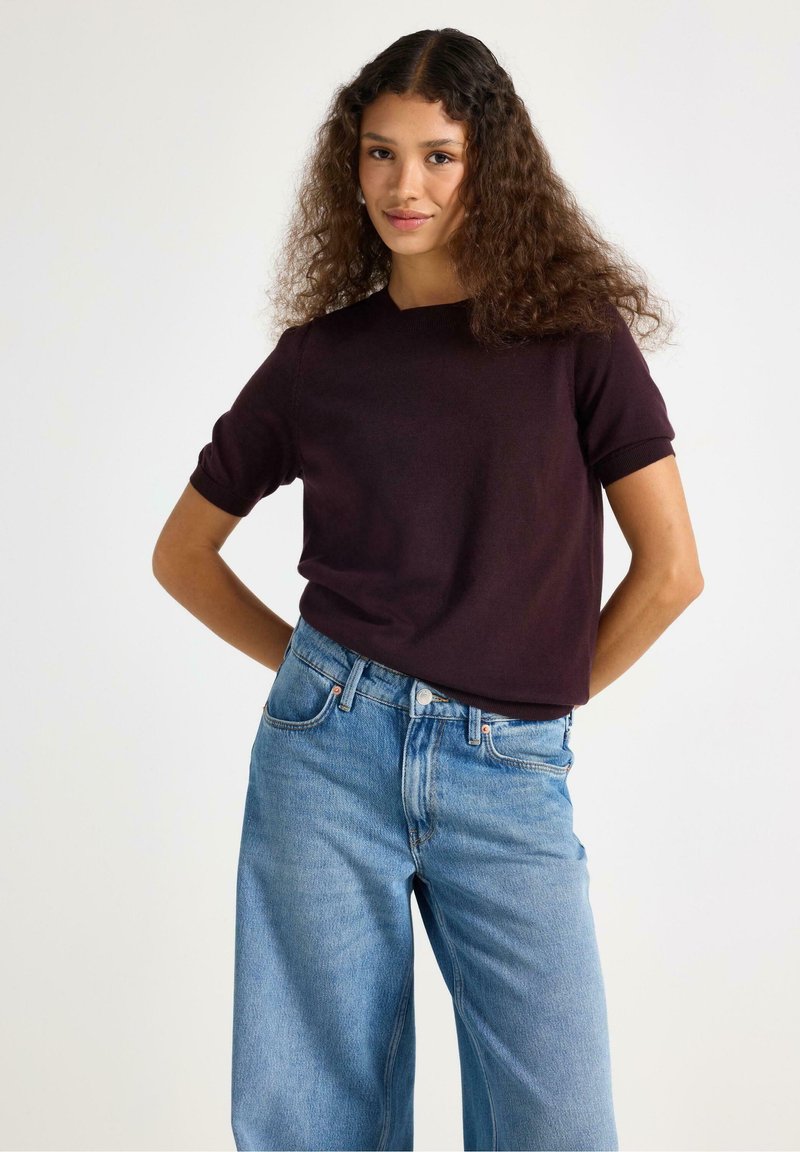 Bordeaux kleurige T-shirt met korte mouwen, gecombineerd met lichtblauwe wijde jeans, met een ontspannen pasvorm en textuur in een minimalistisch ontwerp.