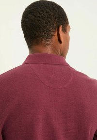 Burgunderfarbenes Polohemd aus strukturiertem Stoff, mit klassischem Kragen und dezentem Logo auf der Rückseite des Kragens.