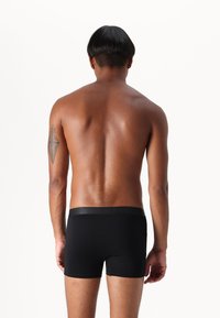 Black boxer briefs with a smooth elastic waistband. The fabric appears stretchy and form-fitting, showcasing a sleek silhouette from the back.