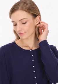 Cardigan bleumarin dintr-un material moale, cu nasturi mici, asemănători cu perlele, pe față și un decolteu rotunjit.