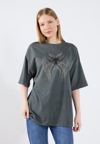 Gray oversized t-shirt with short sleeves, featuring a detailed wing graphic design in lighter shades. Made from soft cotton material.