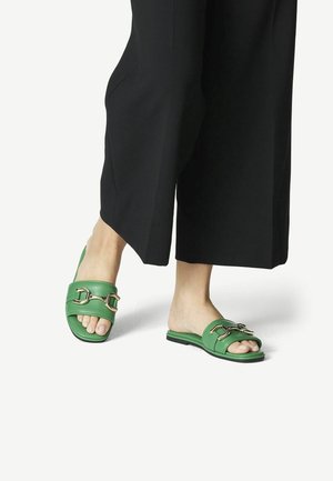 Sandales à glissière vertes avec une finition en cuir lisse, dotées d'un design à double bride et d'accents en métal doré. Portées avec un pantalon large noir.