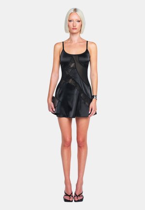 Schwarzes Satin-Kleid mit dünnen Trägern, einem taillierten Oberteil mit durchsichtigen Einsätzen und einem ausgestellten Rock. Begleitet von einer kleinen schwarzen Clutch.