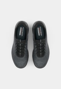 Skechers sneakers in dark gray fabric, featuring a rounded toe, black laces, and a cushioned insole with "Memory Foam" labeling.