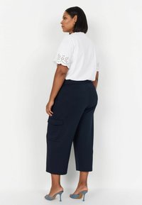 Vit topp med spetsdetaljer, marina cargobyxor med fickor och blå klackmules. Outfiten har en avslappnad passform och mjuka texturer.