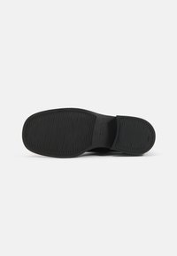 Black shoe sole with textured surface, featuring horizontal and vertical grooves for traction. Rounded toe design with no visible branding.