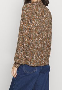 Brown floral blouse with a high neck and gathered cuffs. Features white and green floral patterns against a rich brown background.