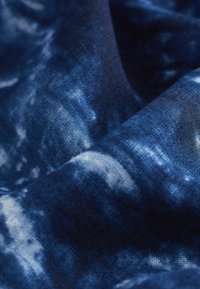 Tessuto in profondo blu con motivi tie-dye in blu più chiaro, che evidenziano una trama liscia e un aspetto tessuto.