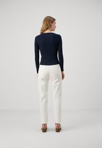 Marineblaues Langarmoberteil mit gerippter Textur, kombiniert mit weißen geraden Hose und beigen Chunky-Heel-Sandalen. Einfaches Dekolleté-Design.