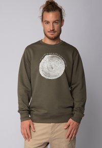 Olijfgroene sweatshirt met een groot wit boomringontwerp met een cirkelvormige textuur en omringende tekst, gemaakt van een lichtgewicht stof.